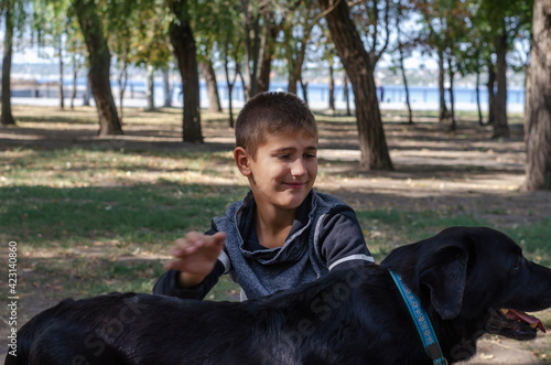 Emotional portrait of a boy stroking a black dog with a blue col © Mikhail