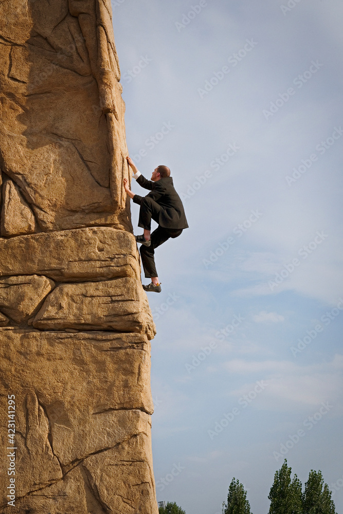 Businessman climbing steep rock face
Businessman climbing steep rock face