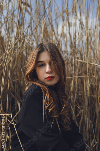 Portrait of a pretty young woman posing outdoors near the lake, dressed in black clothes, high field and sky background.