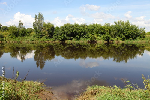 Beautiful European calm Dnieper river landscape with green shores and trees reflection in water surface on blue sky background at Sunny summer day