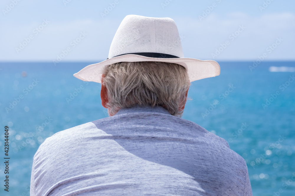 Rear view of gray-haired man with hat looking at horizon over water. Pensioner in sea vacation concept