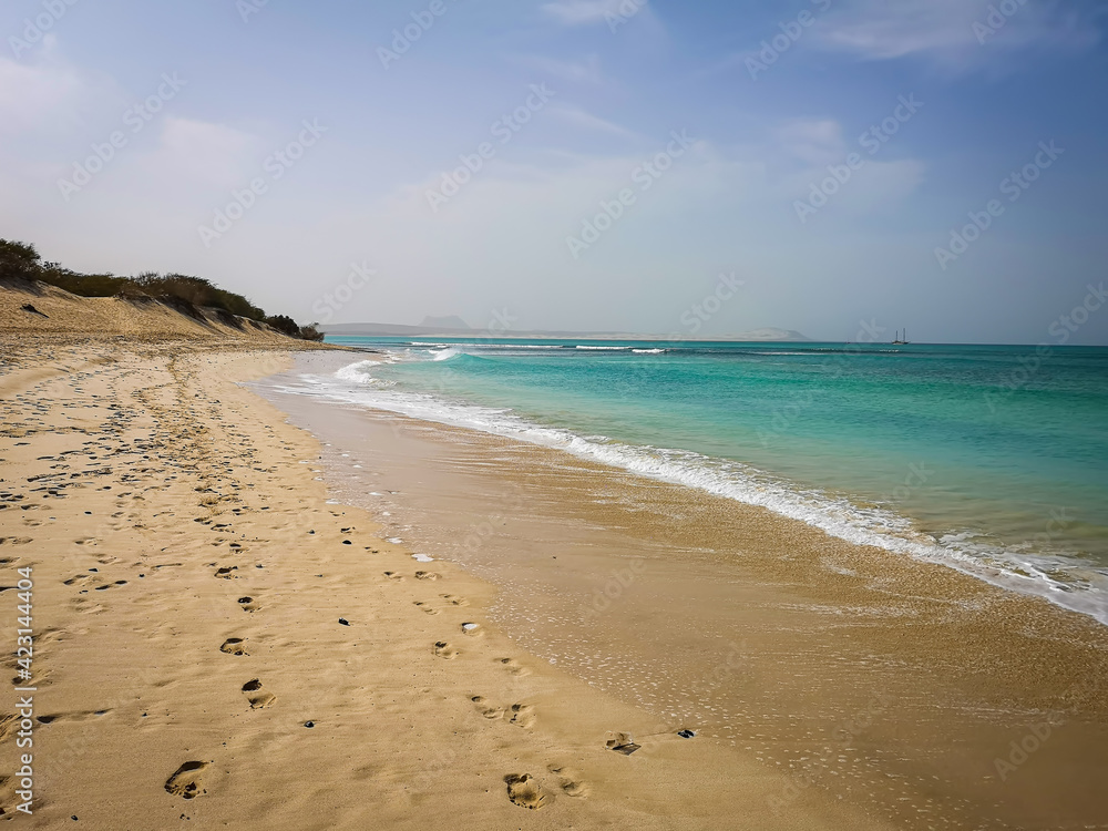 Romantic walk on the beach of Sal Rei, Cape Verde. Footprints in the sand, turquiose water and hot weather. Selective focus on the waves, blurred background.