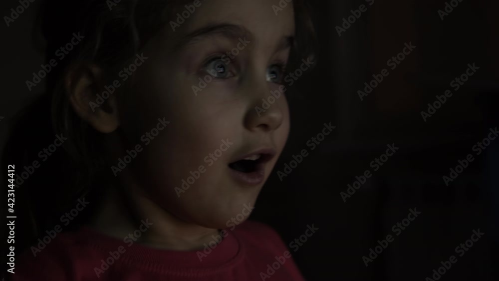 Portrait Сute Little Kid While Watching TV. Young Girl Watch Television on Living Room. Concept Video Game, Entertainment, Emotions, Family. Child Watching TV, Close up Face of Little Girl, Kid Eyes. Portrait Сute Little Kid While Watching TV. Young Girl Watch Television on Living Room. Concept Video Game, Entertainment, Emotions, Family. Child Watching TV, Close up Face of Little Girl, Kid Eyes.
