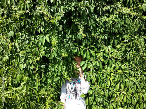 Young woman hiding in hedge from wild grapes