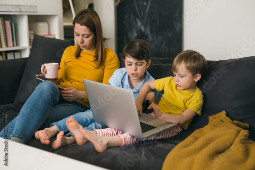 mother and her children using laptop computer while sitting on sofa at home