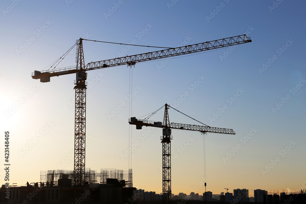 Tower cranes and construction site on sunrise background. Housing development, apartment block in city
