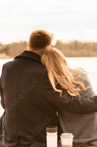 Young couple in love sitting on a terrace and hugging. Couple sitting outside in spring, in front of a lake 