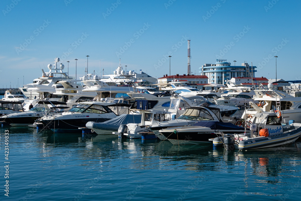 Yachts and boats at pier of Sochi Commercial Sea Port. In background is new Rosmorport building. Center of resort town. Clear sunny winter day. Sochi, Russia - 07 December 2020