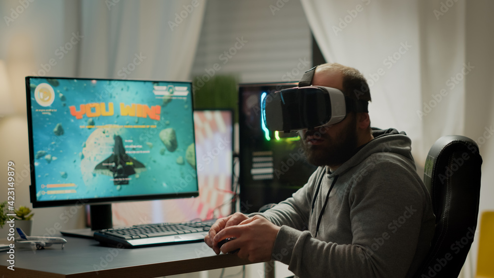Videogame player with VR headset raising hands after winning space shooter competition. Professional pro gamer playing online video games with new graphics on powerful computer from gaming room