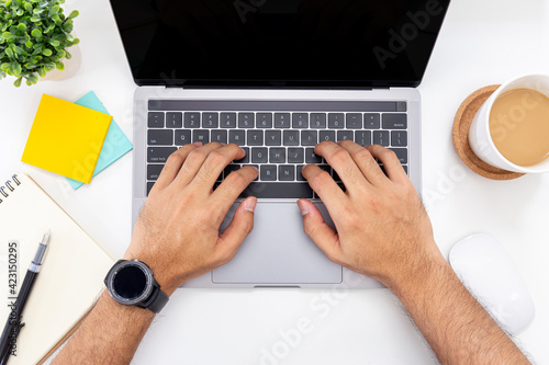 Businessman working on a laptop with coffee cup and notebook with pen on white background, top view
