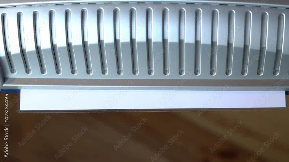 Laminate paper at home in a small laminator. A sheet of white paper in a film crawls out of the device Laminate paper at home in a small laminator. A sheet of white paper in a film crawls out of the device