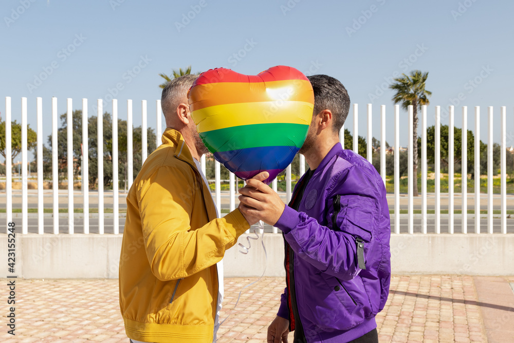 Gay couple behind a heart balloon in rainbow colors