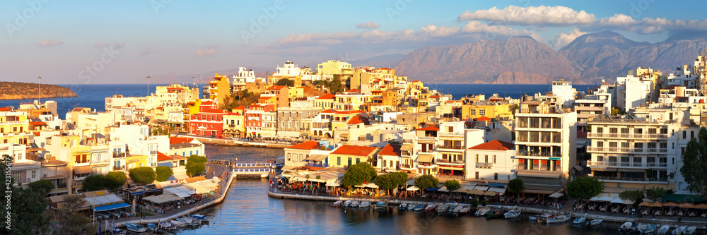 Fototapeta premium Greece. Crete. Panorama of the beautiful southern town of Agios Nikolaos from the top observation deck in the setting sun. Tourists on the embankment are out of focus