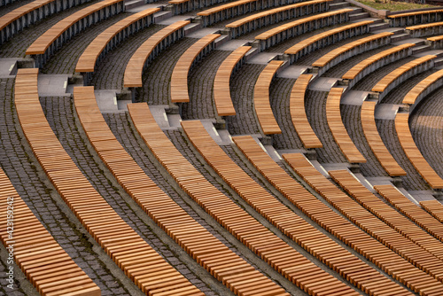 Lots of wooden rounded benches in an empty amphitheater outside in the sunshine by day  © Jakub