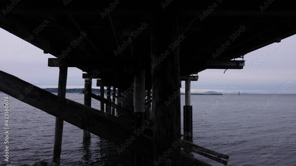 Pan under pier at park with grey sky and clouds in the sky over the ocean horizon dark creepy peaceful Pan under pier at park with grey sky and clouds in the sky over the ocean horizon dark creepy peaceful