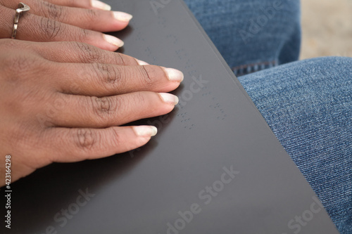 Detail of african american woman´s hands reading braille in a black book.