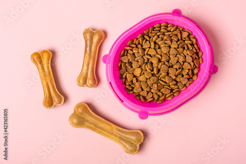 Natural dental bone for dog, dry pieces cat or puppy food in pink plastic bowl isolated on pink background Top view Flat lay Delicious treat for your beloved pet Food, snack for animal concept