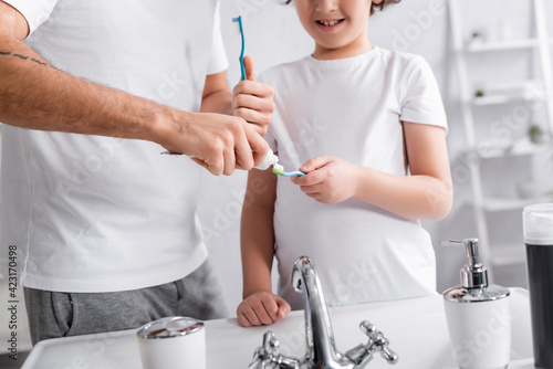 Cropped view of father applying toothpaste on toothbrush near smiling son in bathroom © LIGHTFIELD STUDIOS
