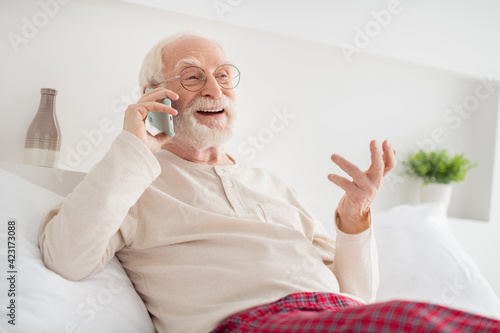 Photo of handsome pretty age pensioner sleepwear spectacles lying bed talking modern device inside indoors home room