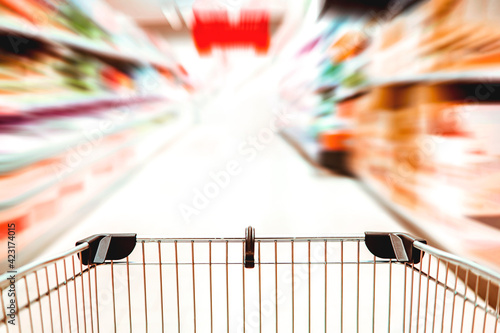 Tableau sur toile Close up of a supermarket trolley in a blurry aisle with motion blur - shopping frenzy and consumerism concept