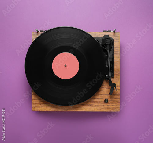 Modern turntable with vinyl record on purple background, top view