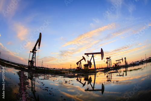 in the evening, oil pumps are running, The oil pump and the beautiful sunset reflected in the water, the silhouette of the beam pumping unit in the evening.