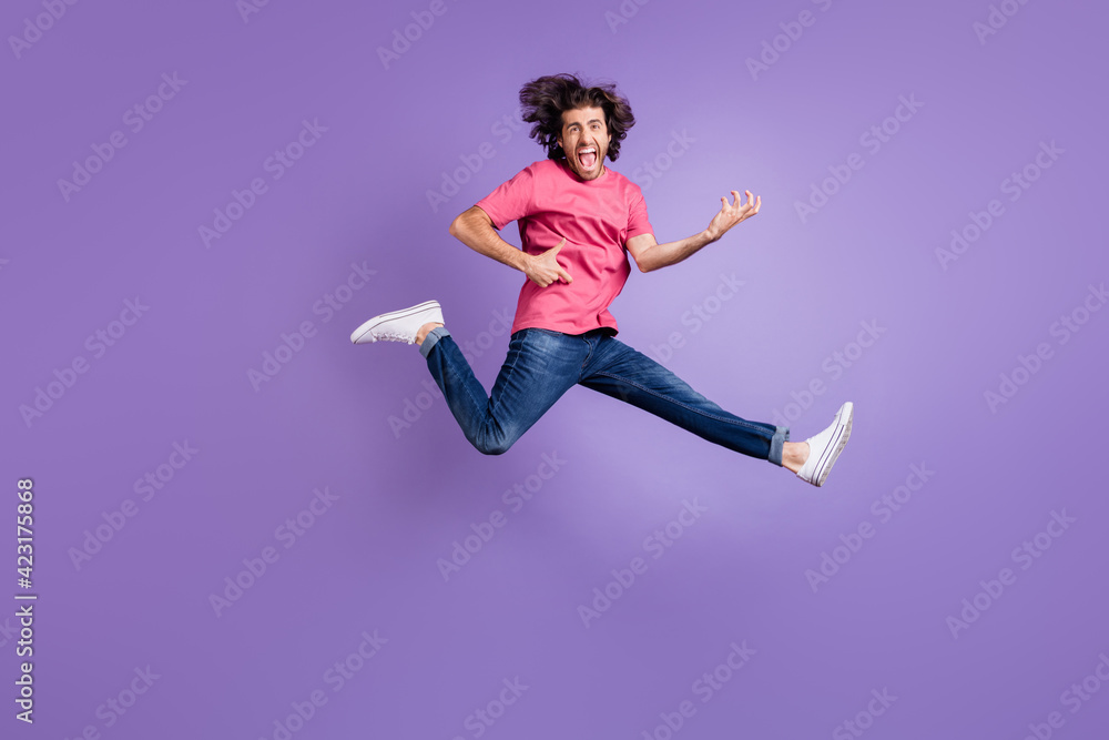 Full length photo of excited cool young guy dressed pink outfit jumping high playing guitar isolated purple color background