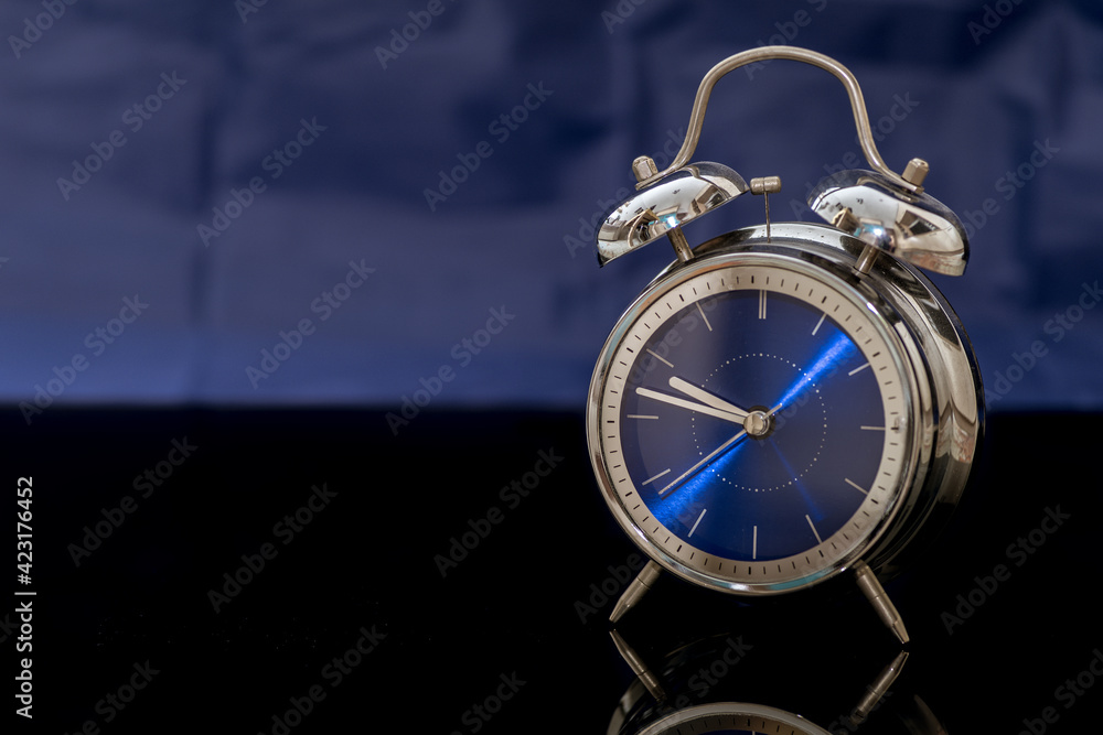 Fototapeta premium budzik z niebieską tarczą na niebiesko-czarnym tle