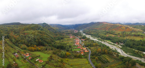 Aerial drone view of Novaci village and Gilort river Valley in a cloudy day. The Parang Mountains Massif  in the background is covered by fog. Autumn season. Romania  photo