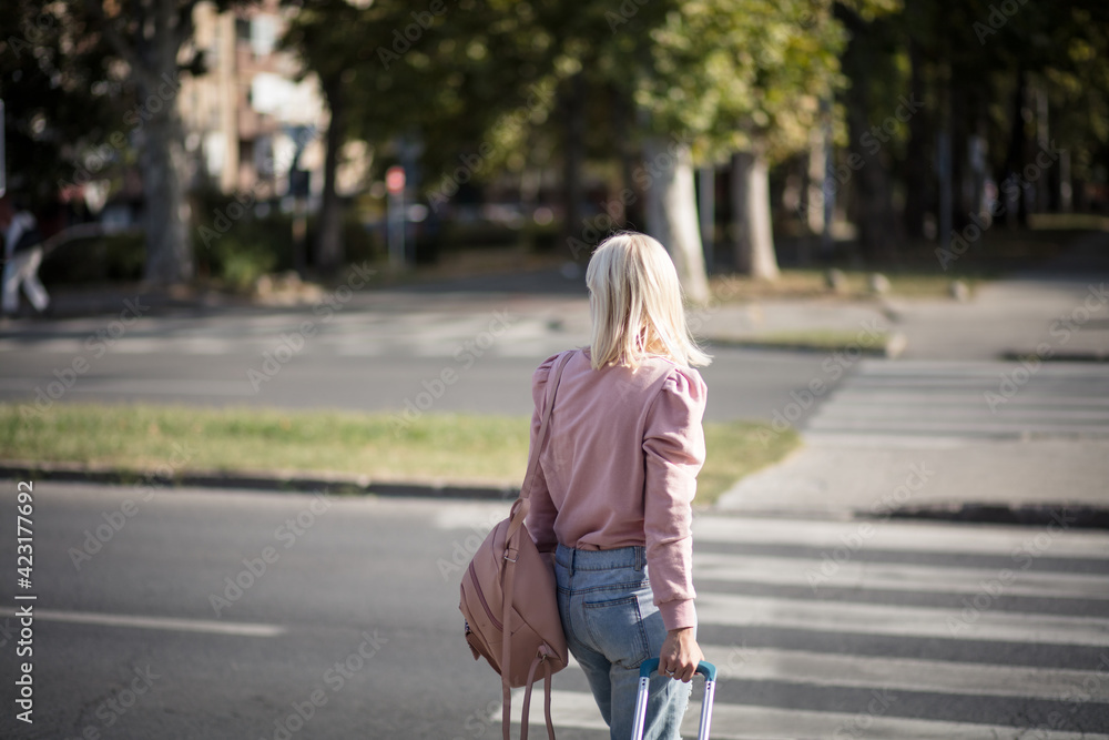 Blond woman with suitcase crossing the road.