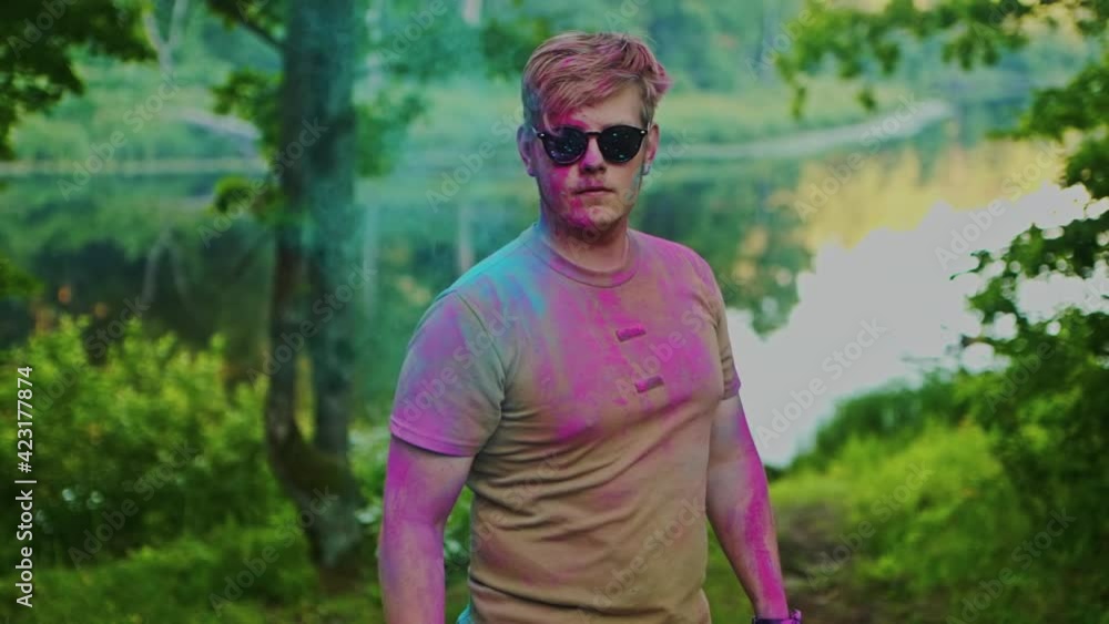 A young handsome man in sunglasses pours blue powder over himself A young handsome man in sunglasses pours blue powder over himself