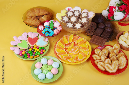 Sweets, candies, chocolate, marmalade, marshmallows, cookies in saucers on a yellow background. 