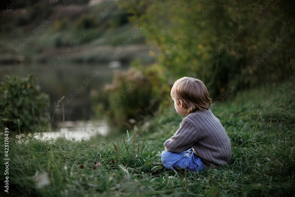 Sad boy child in sweaters on the shore of the lake, a child look at the water. Concept Children's Emotions and Security Sad boy child in sweaters on the shore of the lake, a child look at the water. Concept Children's Emotions and Security