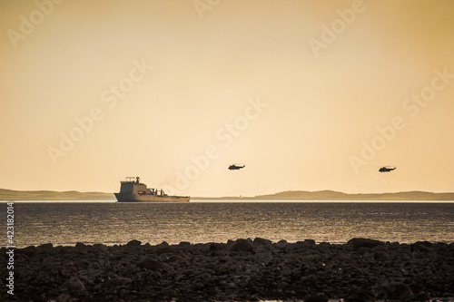 helicopters fly above warship