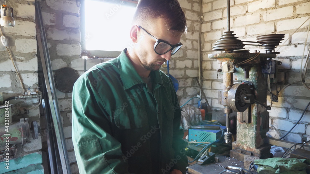 Male mechanic in uniform working with metal details in workshop. Young repairman in protective eyewear doing his job in garage. Concept of maintenance service. Close up Slow motion
