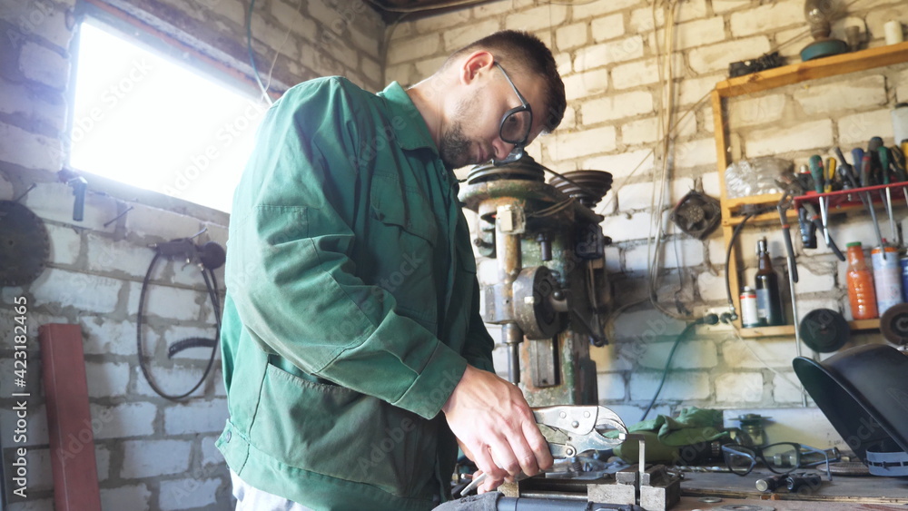 Young repairman in workwear using pliers for fixing metal part on table at workshop. Male mechanic in protective glasses working in garage. Concept of maintenance service. Close up Slow motion Young repairman in workwear using pliers for fixing metal part on table at workshop. Male mechanic in protective glasses working in garage. Concept of maintenance service. Close up Slow motion