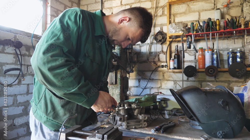 Male mechanic in uniform repairing vehicle detail using tool at workshop. Professional repairman in workwear working at his garage. Concept of maintenance service. Crane shot Slow motion Male mechanic in uniform repairing vehicle detail using tool at workshop. Professional repairman in workwear working at his garage. Concept of maintenance service. Crane shot Slow motion