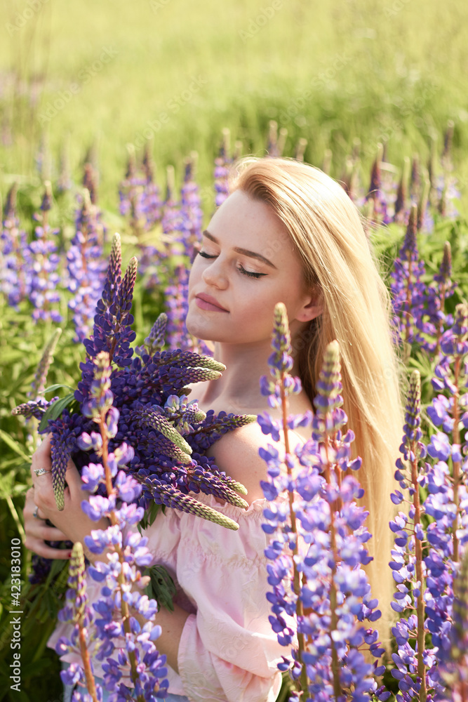 Young attractive long-haired blonde with a bouquet of lupins among a purple field. The concept of nature and romance. Young attractive long-haired blonde with a bouquet of lupins among a purple field. The concept of nature and romance.