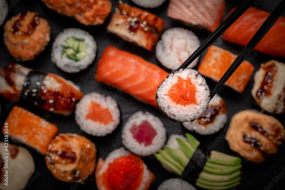 Assorted sushi nigiri and maki big set on slate. A variety of Japanese food with tuna, crab, salmon, eel and rolls. Take sushi in chopsticks Assorted sushi nigiri and maki big set on slate. A variety of Japanese food with tuna, crab, salmon, eel and rolls. Take sushi in chopsticks