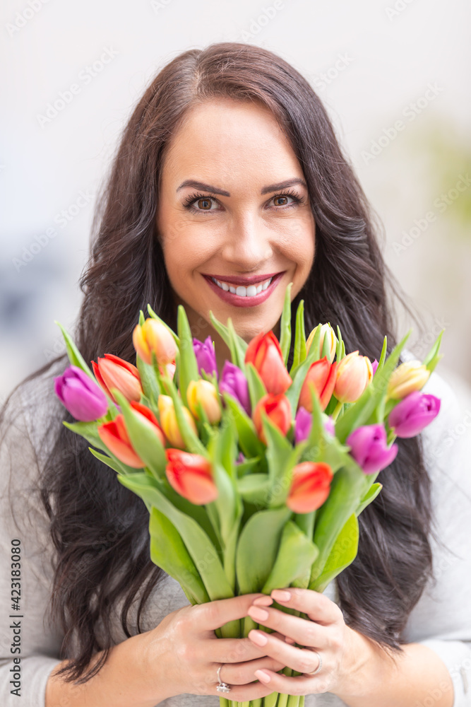 Happy dark haired woman holding in hands a lovely bouquet full of tulips during national womens day Happy dark haired woman holding in hands a lovely bouquet full of tulips during national womens day