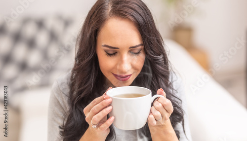 Bilde på lerret Young brunette woman holding a cup of tea or coffee and smelling lovely aroma