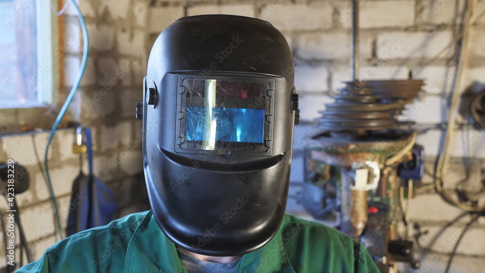 Happy young repairman opening protective mask and showing grimaces into camera. Portrait of mechanic in uniform making funny face and fooling around in garage. Welder with beard working in workshop Happy young repairman opening protective mask and showing grimaces into camera. Portrait of mechanic in uniform making funny face and fooling around in garage. Welder with beard working in workshop