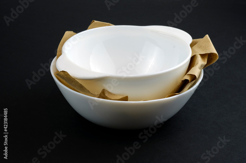 Two deep white ceramic plates stacked one on top of the other. Tureens new with wrapping paper on a black background. White crockery made of impact-resistant material. photo