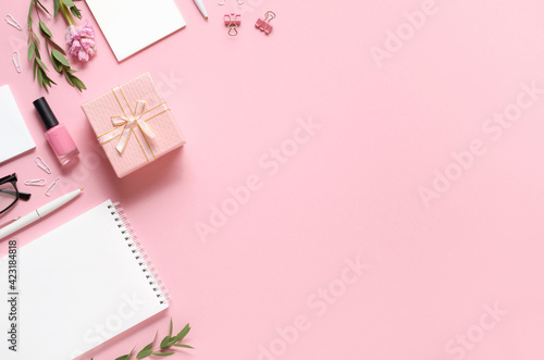 Workplace with notepad, pen, gift and other accessories on pink background