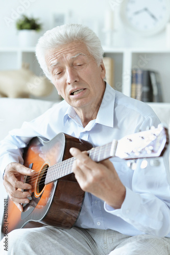 happy senior man with guitar sitting on the sofa at home