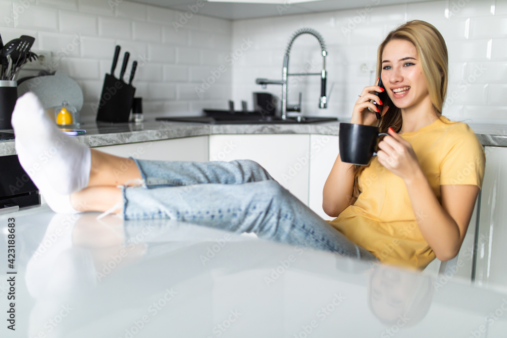 Portrait of young woman talking cell phone, drink coffee or tea in the kitchen Portrait of young woman talking cell phone, drink coffee or tea in the kitchen