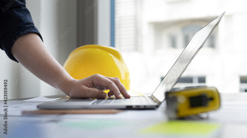 Young man with a laptop plotting a system of building structures in blueprints, Architects or engineers are designing buildings using computers to calculate the physical structure to be correct. Young man with a laptop plotting a system of building structures in blueprints, Architects or engineers are designing buildings using computers to calculate the physical structure to be correct.