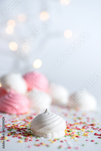 White and pink meringue background with decoration and backlights. Front view. Macro photography. Vertical.
