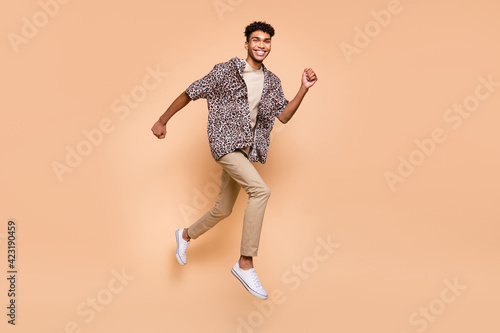 Full size profile photo of brunet optimistic guy run jump wear modern shirt pants isolated on beige color background
