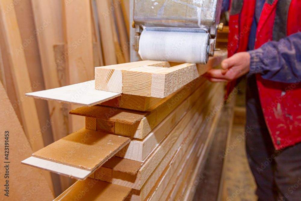 Carpenter smears the boards with hand roller tool, spreader for evenly application of glue on the wooden surface